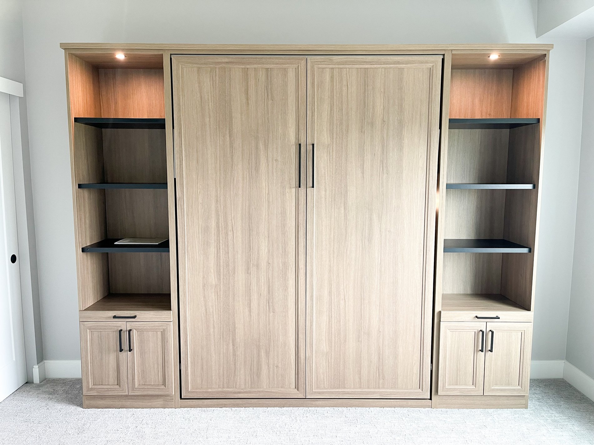 Simple and functional wall bed designed in a mid tone wood grain finish with black open shelves and lighting.