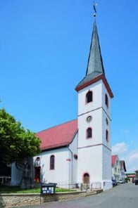 Außenansicht der weißen Kirche mit spitzem, dunklen Kirchturm.
