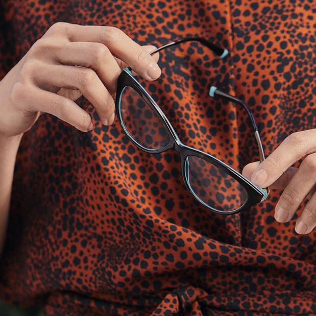 Woman in cheetah print shirt holding prescription eyeglasses