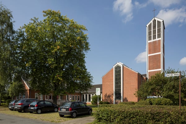 Kirchgebäude und Kirchturm aus Backsteinen mit Parkplatz vor dem Gebäude.