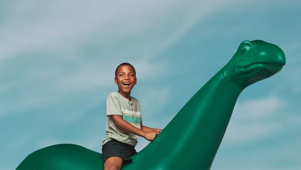 Smiling child sitting on a green fiberglass dinosaur statue.