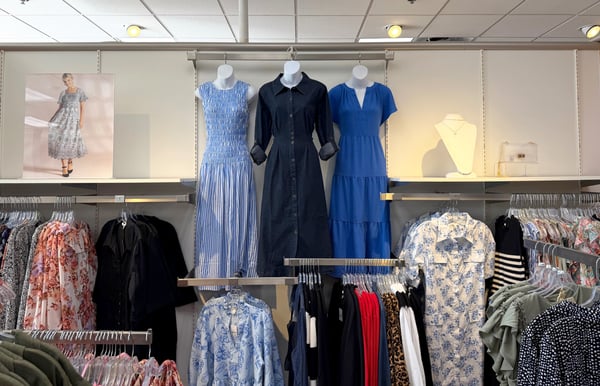 Three blue dresses are displayed on dress forms hanging on the wall, surrounded by affordable and flattering dresses for all sizes at Cato Fashions.