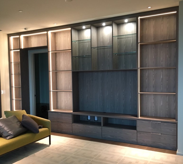 Dark colored media center and bookshelf includes accent lighting, glass shelves and cubbies in a lighter finish.