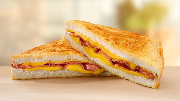 A Bacon & Cheese Toasted Sandwich on a brown surface with a blurred background.