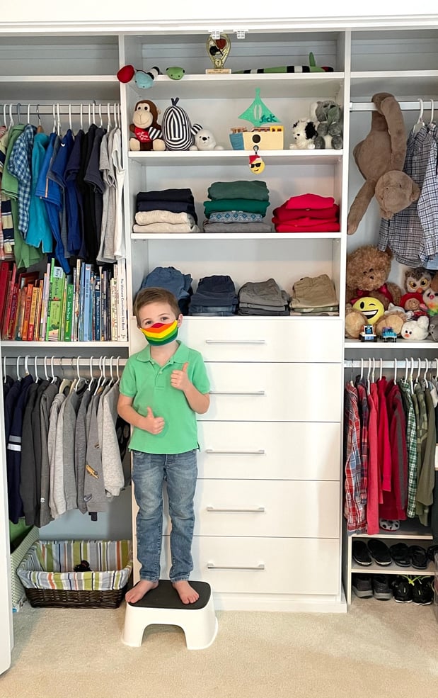 kid's reach-in closet in white with drawers in center and kid on stool with rainbow face mask