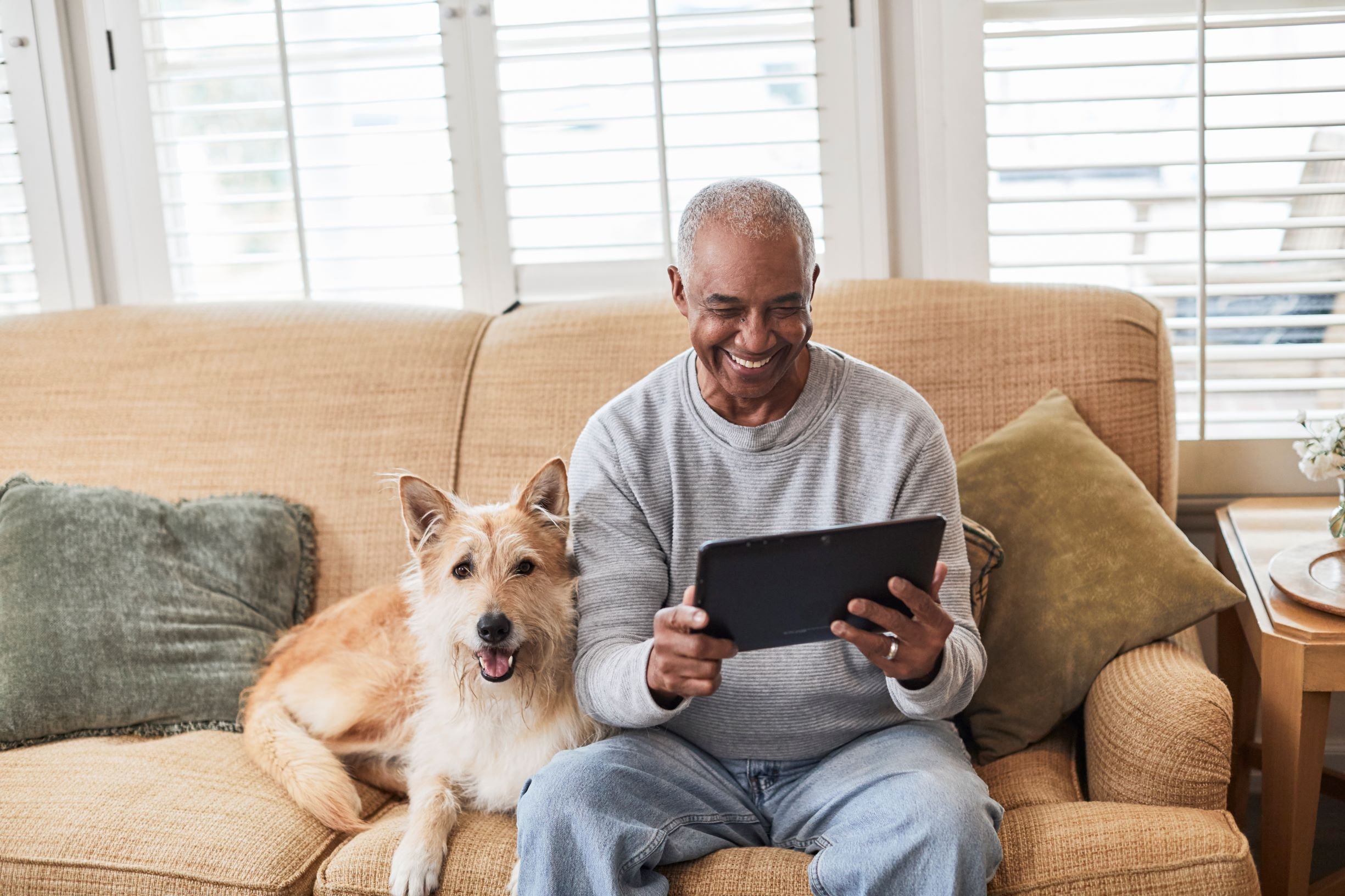 Senior man using tablet on couch with dog