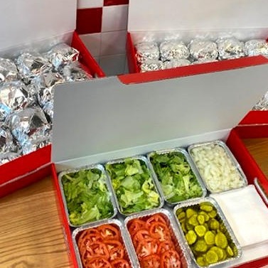 Catering boxes of Five Guys burgers and toppings.