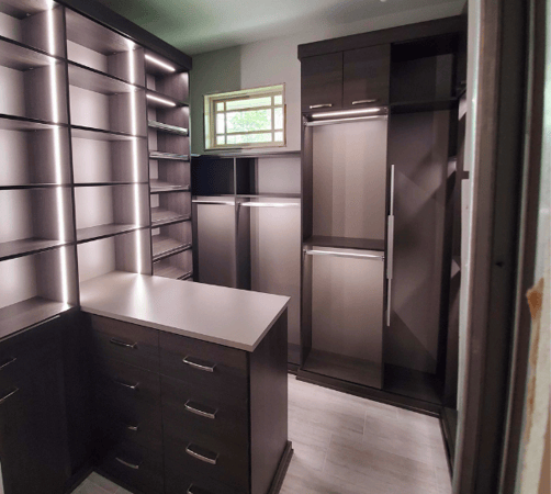 Custom closet with shelving, hanging space, drawers, and accent lighting.