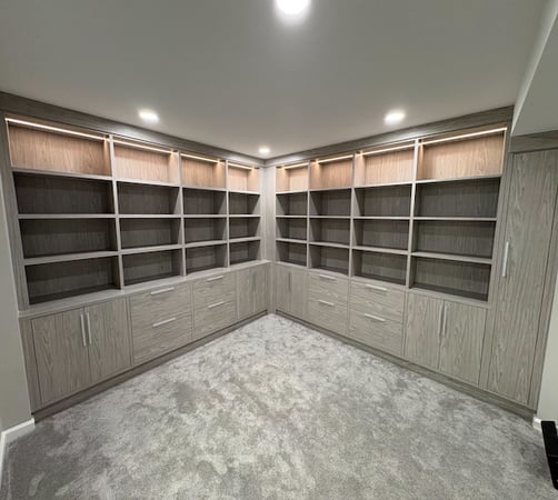 Custom home library featuring built-in cabinets, floating shelves, drawer organization, and integrated lighting for elevated living room storage and home organization. This custom storage system by California Closets includes floor-to-ceiling shelving, custom cabinetry, and organized display storage designed for books, décor, and functional everyday use in Birmingham, Michigan