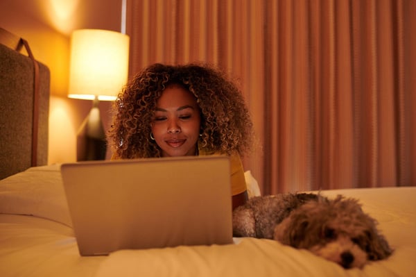 Mujer recostada en la cama con su computadora portátil usando Wi-Fi junto a su perro