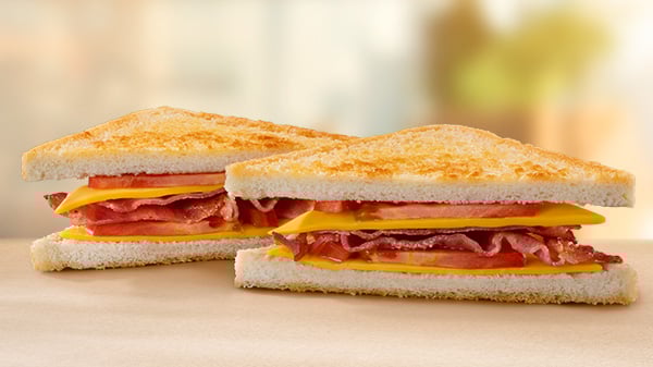 A Bacon, Cheese & Tomato Toasted Sandwich on a brown surface with a blurred background.