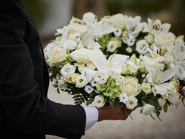 A white funeral wreath held by an arranger