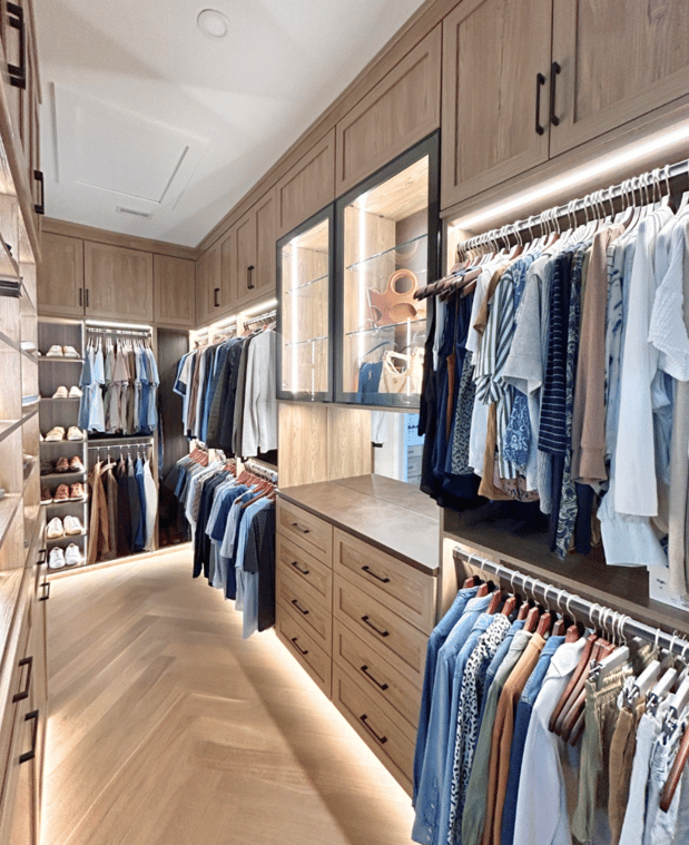Custom walk-in closet with wood cabinetry, hanging storage, drawers, shoe shelving, and illuminated glass cabinets.
