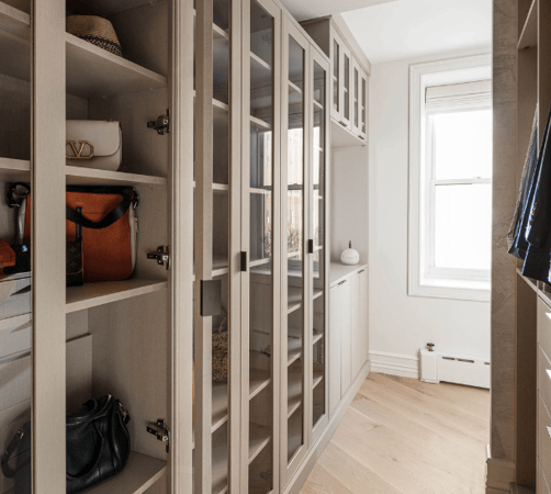 beige custom walk-in closet with glass doors, vanity, purse storage