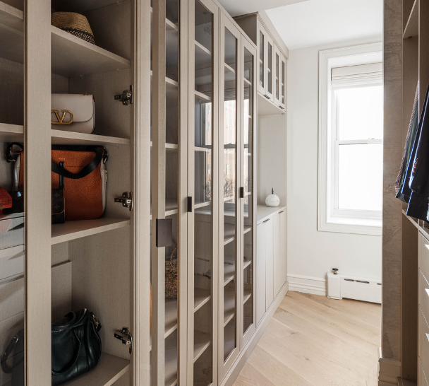 beige custom walk-in closet with glass doors, vanity, purse storage