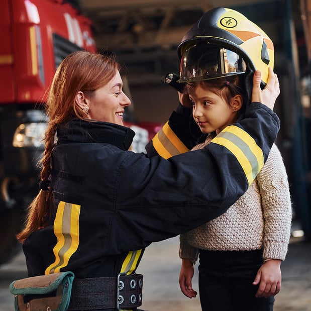 A female firefighter placing a helmet on a young girl