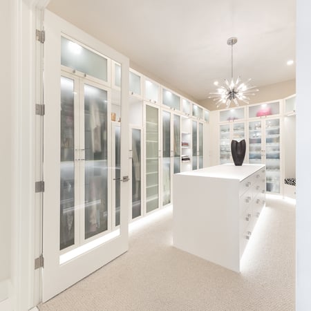 White walk-in closet with floor to ceiling glass cabinetry, center island, and under-cabinet lighting by California Closets Edmonton, Alberta.