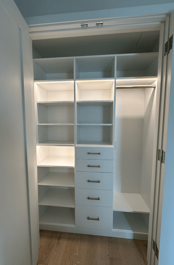 California Closets New York white custom reach-in closet with LED lighting, hanging, shelving, and drawer space