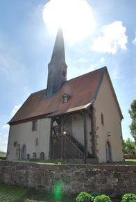 Das Bild zeigt die Außenansicht der Evangelischen Nikolaikirche Hartershausen. Die Kirche ist von einer circa ein Meter hohen Mauer umrundet.