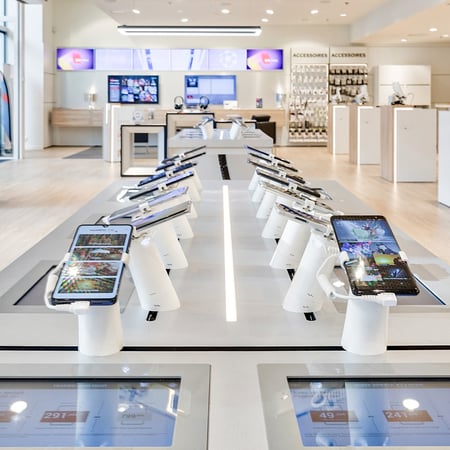 IPads and smart phones sit in white display stands on a long table inside a SFR showroom