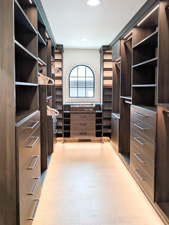 Dark brown walk in closet with lighting, hanging, drawers, and open shelving.