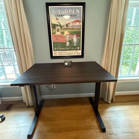 Virginia Beach – Embedded plugs – Dark wood adjustable desk beneath framed U.S. Open poster