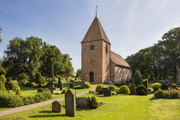 Ein Kirchengebäude umringt von einem begrünten Friedhof.