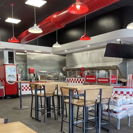 A photograph of the dining room, including a look at the Coca-Cola Freestyle machine and high-top tables, inside the Five Guys restaurant at 1314 Commons Drive in Geneva, Illinois.