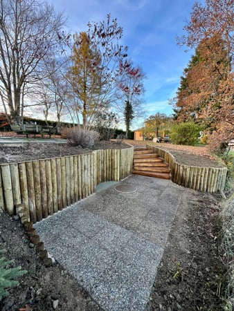 Thury Paysagiste & Services – Rénovation complète des extérieurs à Auboranges dans le canton de Fribourg : réfection de l’escalier en bois, remplacement du soutènement en rondins et remise en état de la terrasse.