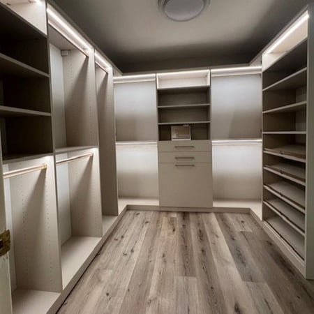Spacious custom walk-in closet with open shelving, hanging storage, built-in drawers, shoe shelves, and integrated lighting.