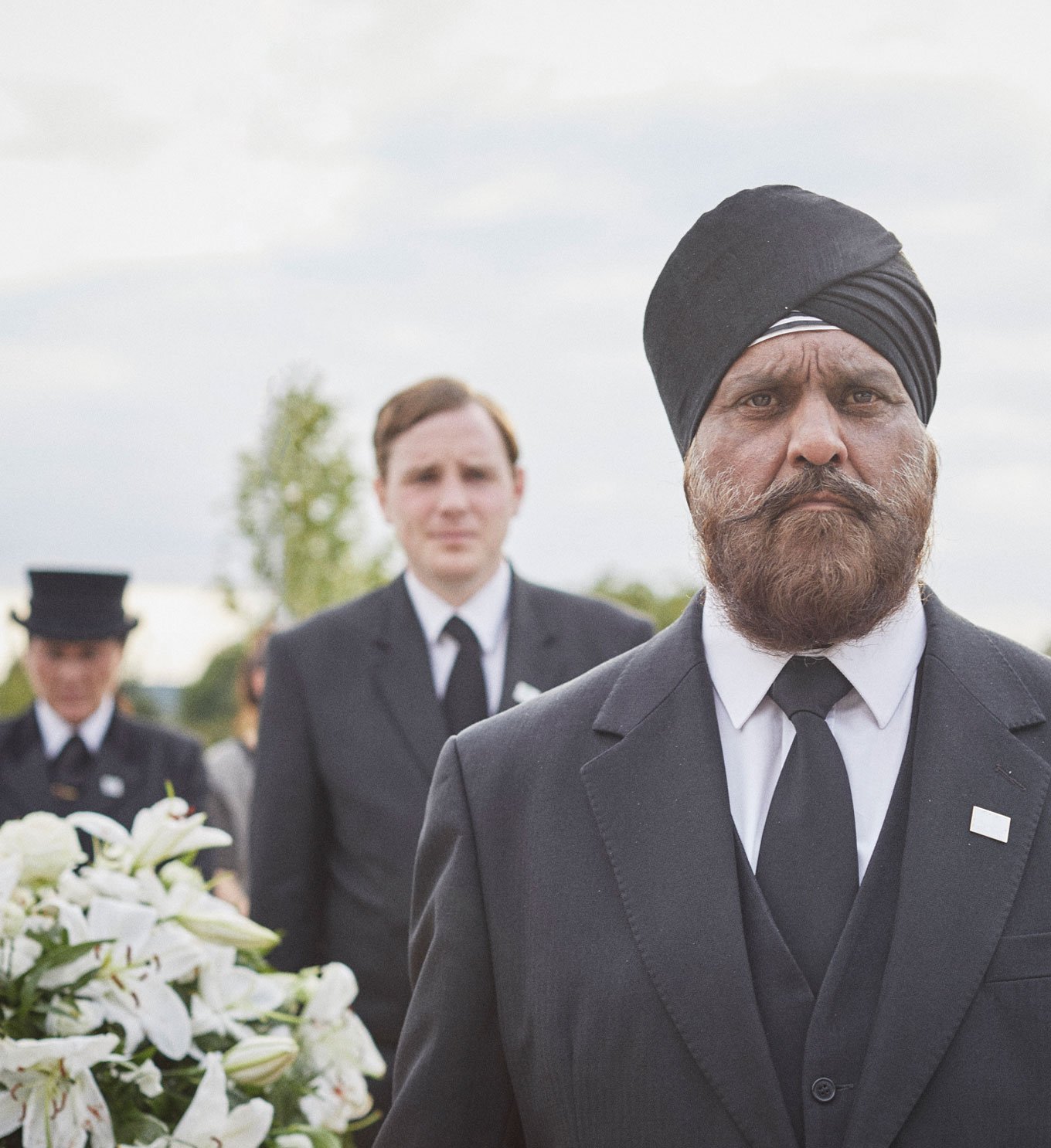 A Sikh funeral director wearing a turban helps to bear a coffin for a traditional funeral