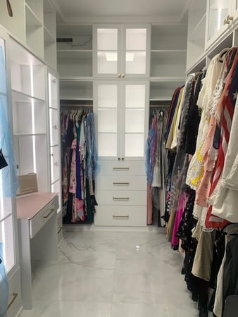 Master closet with Dove finish, Swagger gold hardware, clear glass inserts, and petal pink matte glass countertop.