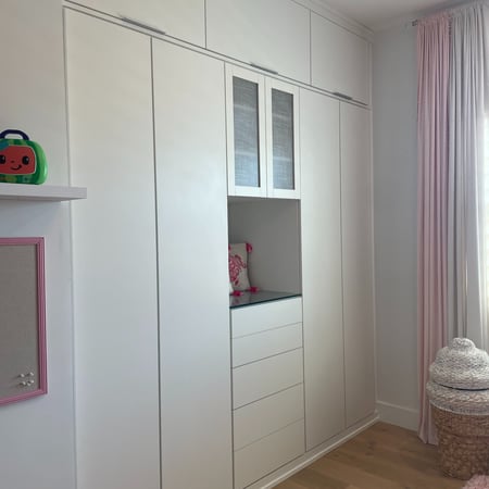 White floor-to-ceiling built-in cabinetry with concealed storage, drawers, and open display shelving in a bright interior.