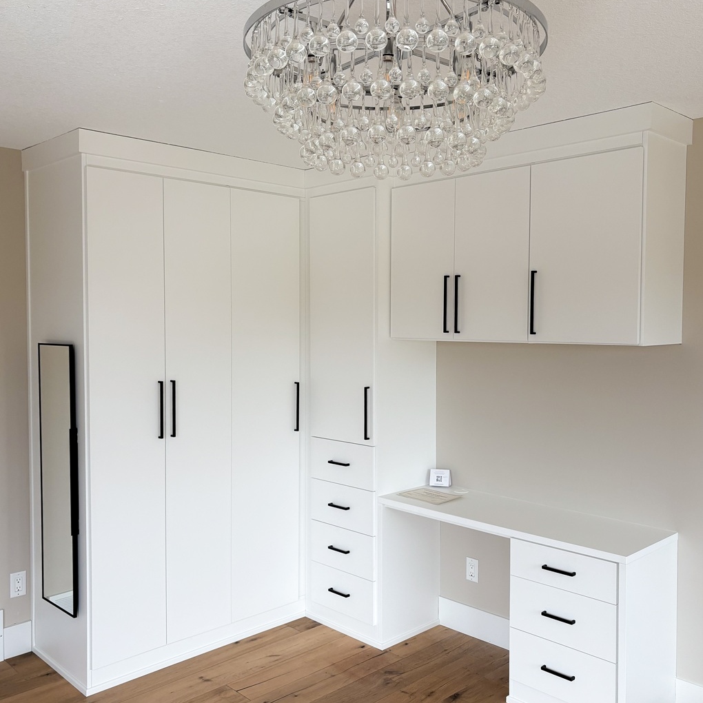 White wardrobe system with vanity. Floor to ceiling storage with modern crown moulding, black hardware, and black pull out mirror.