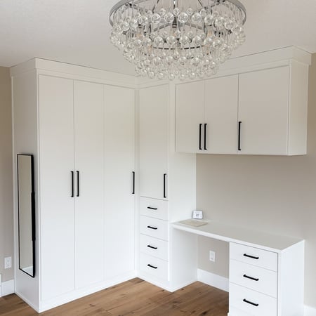 White wardrobe system with vanity. Floor to ceiling storage with modern crown moulding, black hardware, and black pull out mirror.