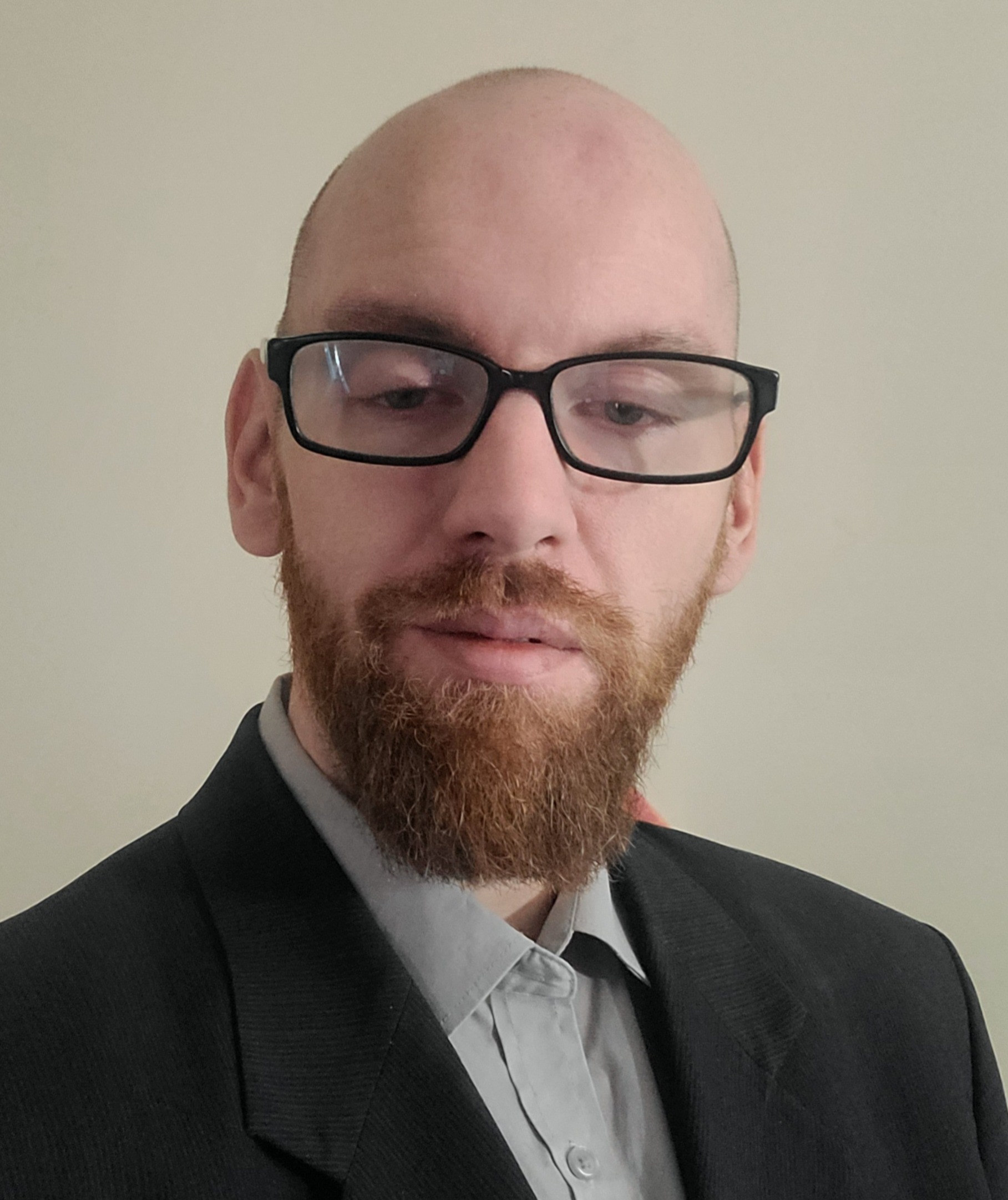 Dave Miller, bald, black thick-rimmed glasses with beard. Wearing suit jacked and blue-grey shirt