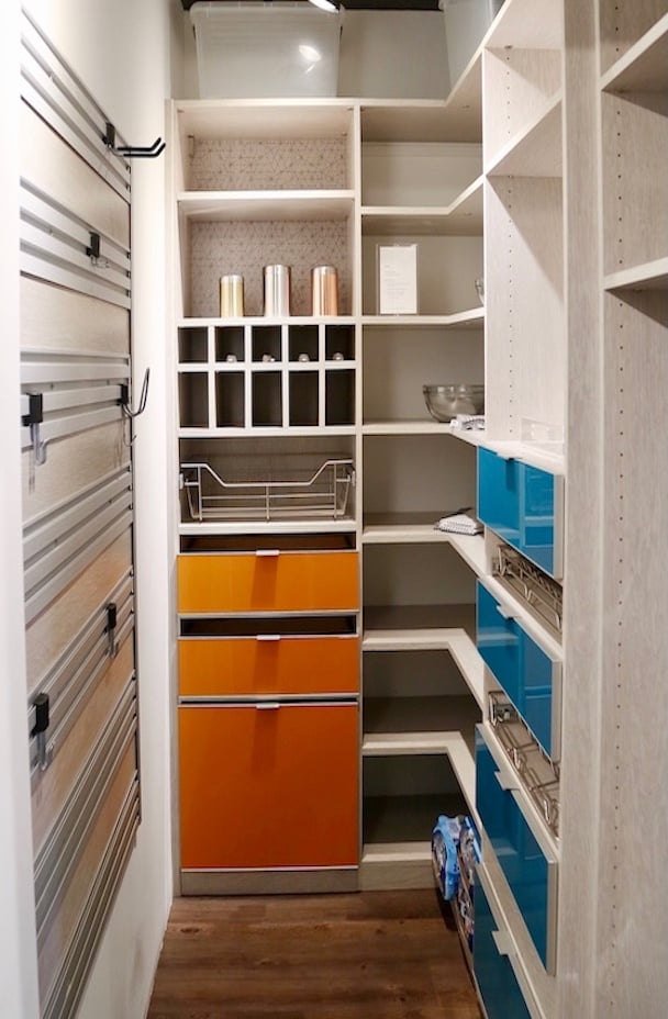 Custom pantry with a fusion track wall, pull out wire baskets, and blue and orange cabinets