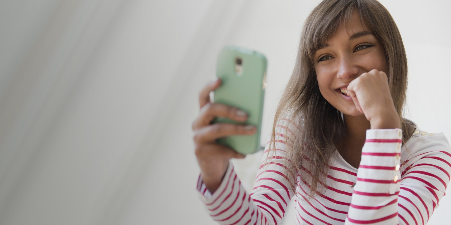 Foto de una mujer joven sonriendo a su teléfono inteligente conectado a Optimum Mobile