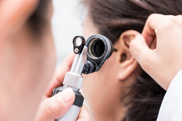 Audiologist uses an otoscope to check for fluid in his patient's ear.