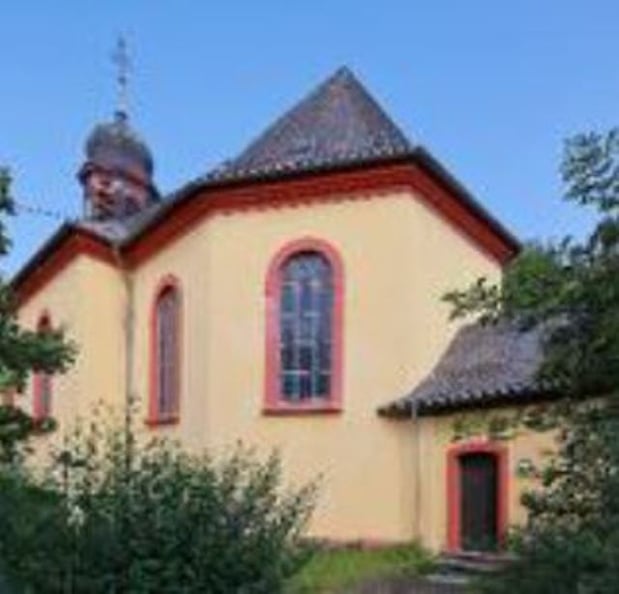 Außenansicht der Kirche Gensingen. Die prägenden Farben sind beige und das Dach sowie der die Turmspitze sind schwarz.