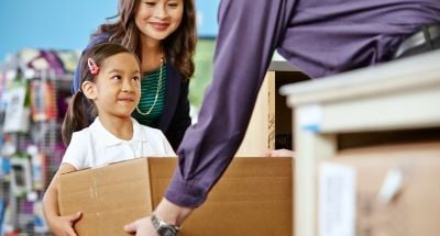 A mother and daughter smile while dropping off a package for an easy Amazon Return at a FedEx Office counter.