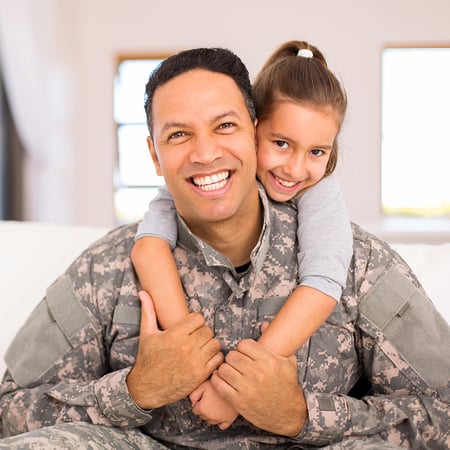 A young girl with her arms around a man in a camo uniform