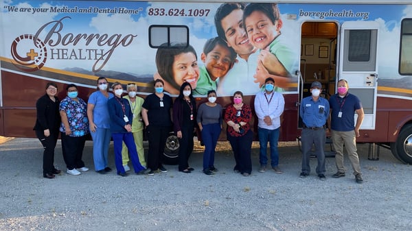 Masked Borrego Health employees stand outside a Borrego Health mobile unit