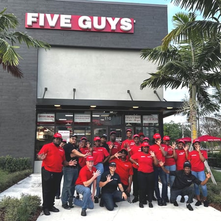 Employees pose for a photograph outside the entrance to the Five Guys restaurant at 1700 NE 23rd St. in Pompano Beach, Florida.