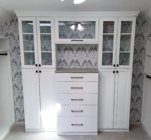 white wardrobe with drawers and cabinets with glass doors and blue and grey wallpaper