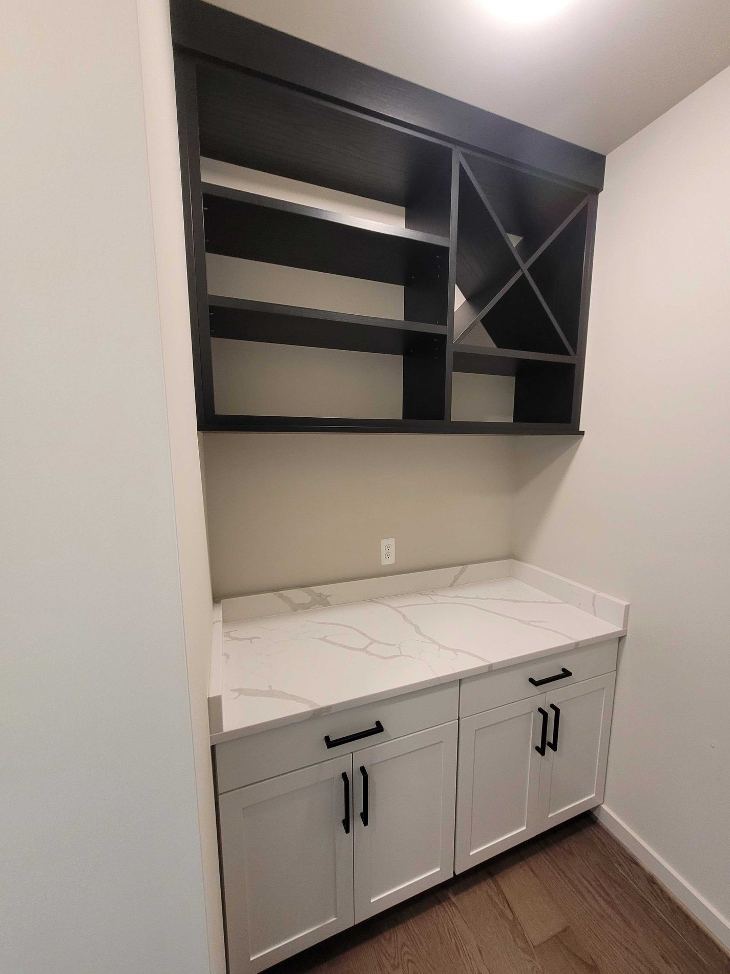 Home bar with white lower cabinets and shadow black upper unit with a wne cross and shelves