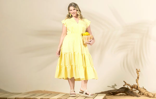 Woman is wearing a yellow plus size midi dress and holding a basket of lemons.