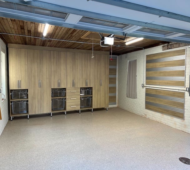 Custom garage storage with woodgrain cabinets, pull-out baskets, and fusion track wall