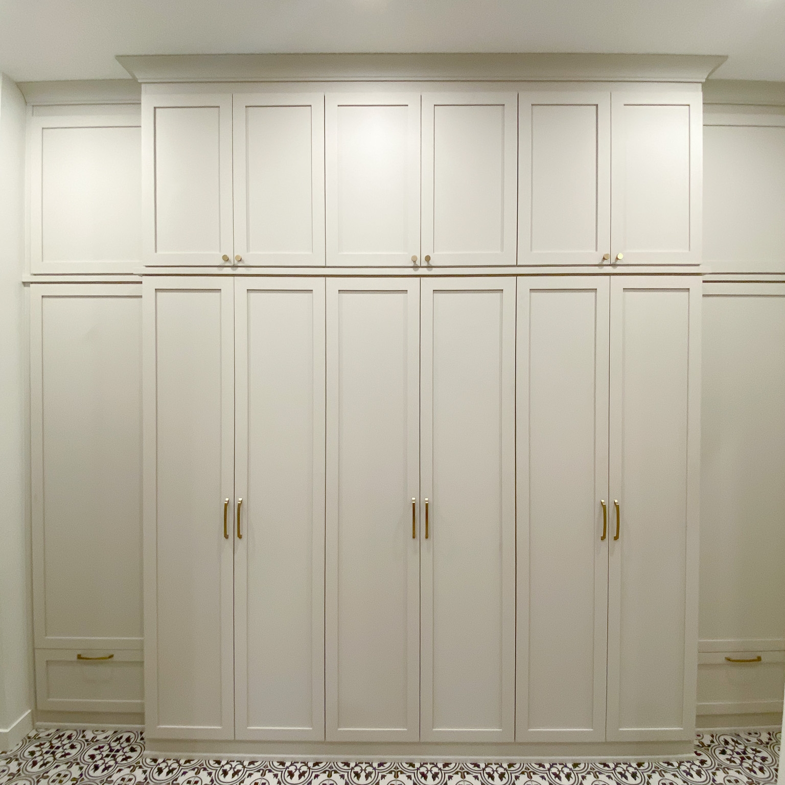 White floor to ceiling mudroom with shaker doors and gold hardware.