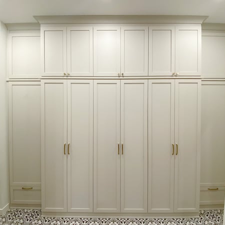 White floor to ceiling mudroom with shaker doors and gold hardware.